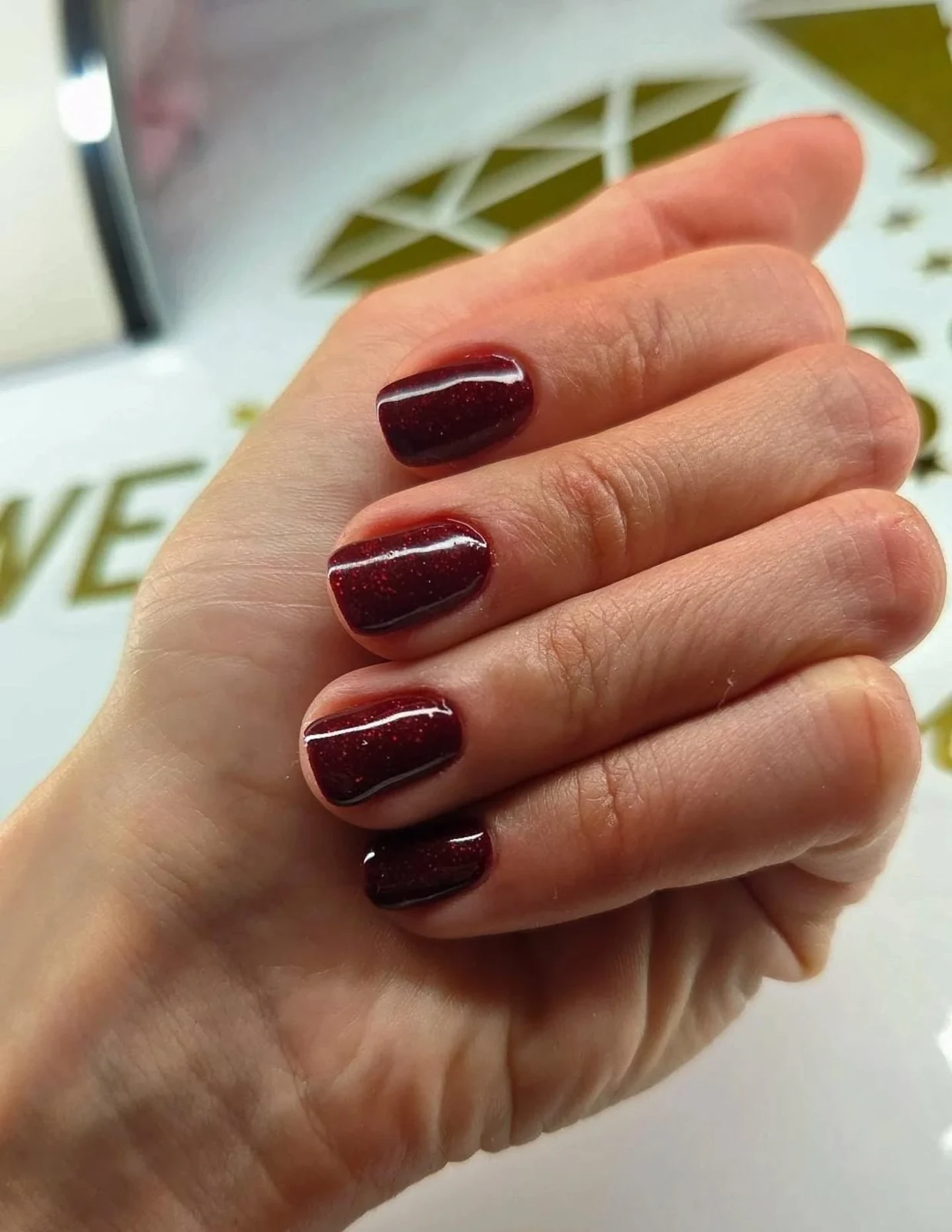 Manikura bordo s odsjajem na Wellness Beauty logotipu